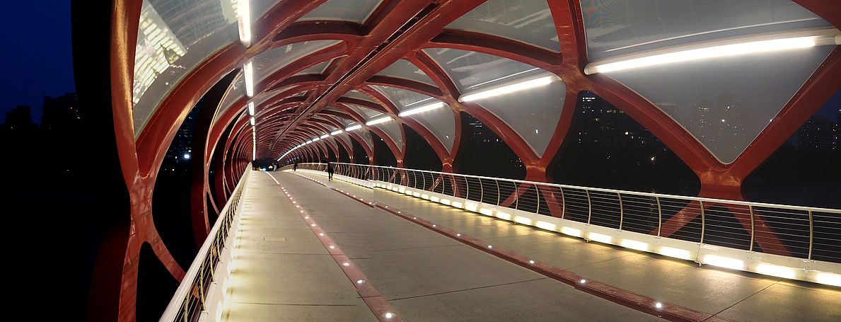 Structure tubulaire et illuminée du Peace Bridge de Calgary à la tombée de la nuit.