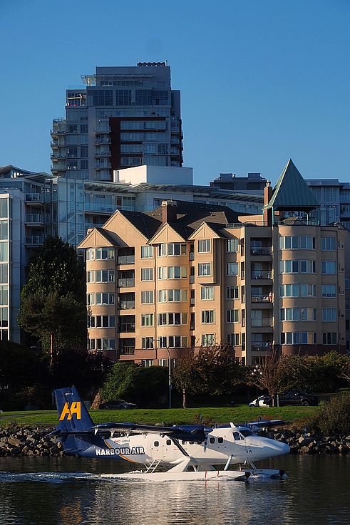 Harbour Air seaplane navigating James Bay in Victoria, in front of residential buildings.
