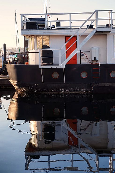 Reflection of a floating house with an orange door in Victoria's harbor.