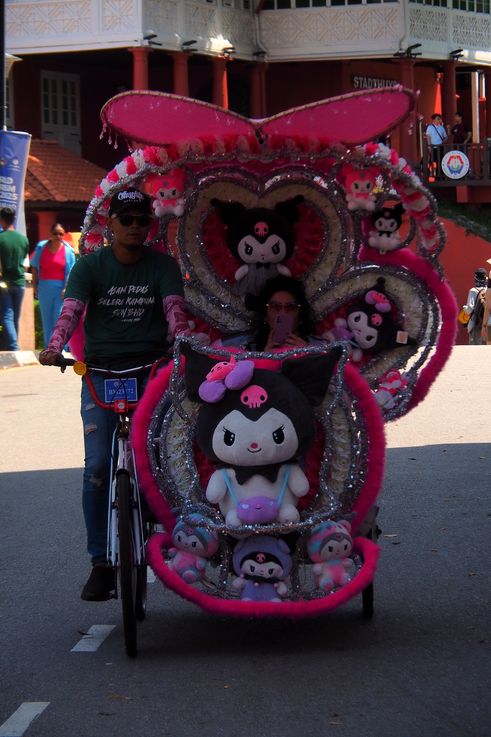 Trishaw decorado con personajes de Kuromi frente al Stadthuys de Melaka.