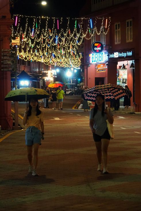 Calle iluminada de la Plaza Holandesa de Melaka, por la noche, con paraguas.