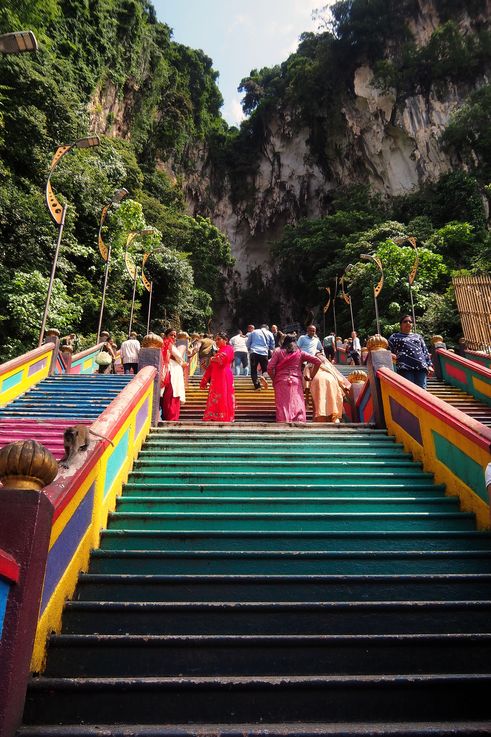 Colorful staircase of the Batu Caves temple, with visitors and a long-tailed macaque.